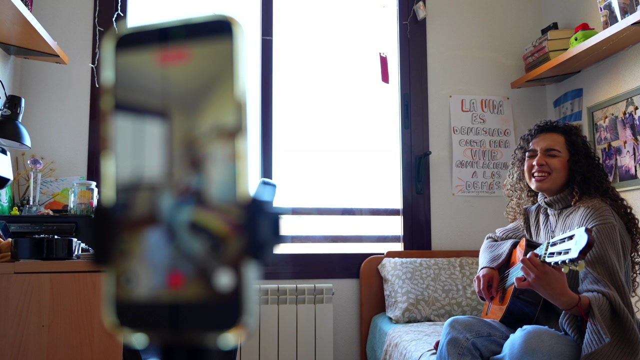 Musicista creativa che canta e suona la chitarra mentre registra un vlog nella sua camera da letto per i social media.