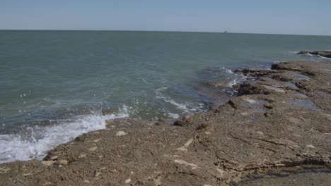 Ola-De-Mar-Limpia-Y-Tranquila-Golpeando-Rocas-Con-Un-Barco-Distante-En-El-Océano