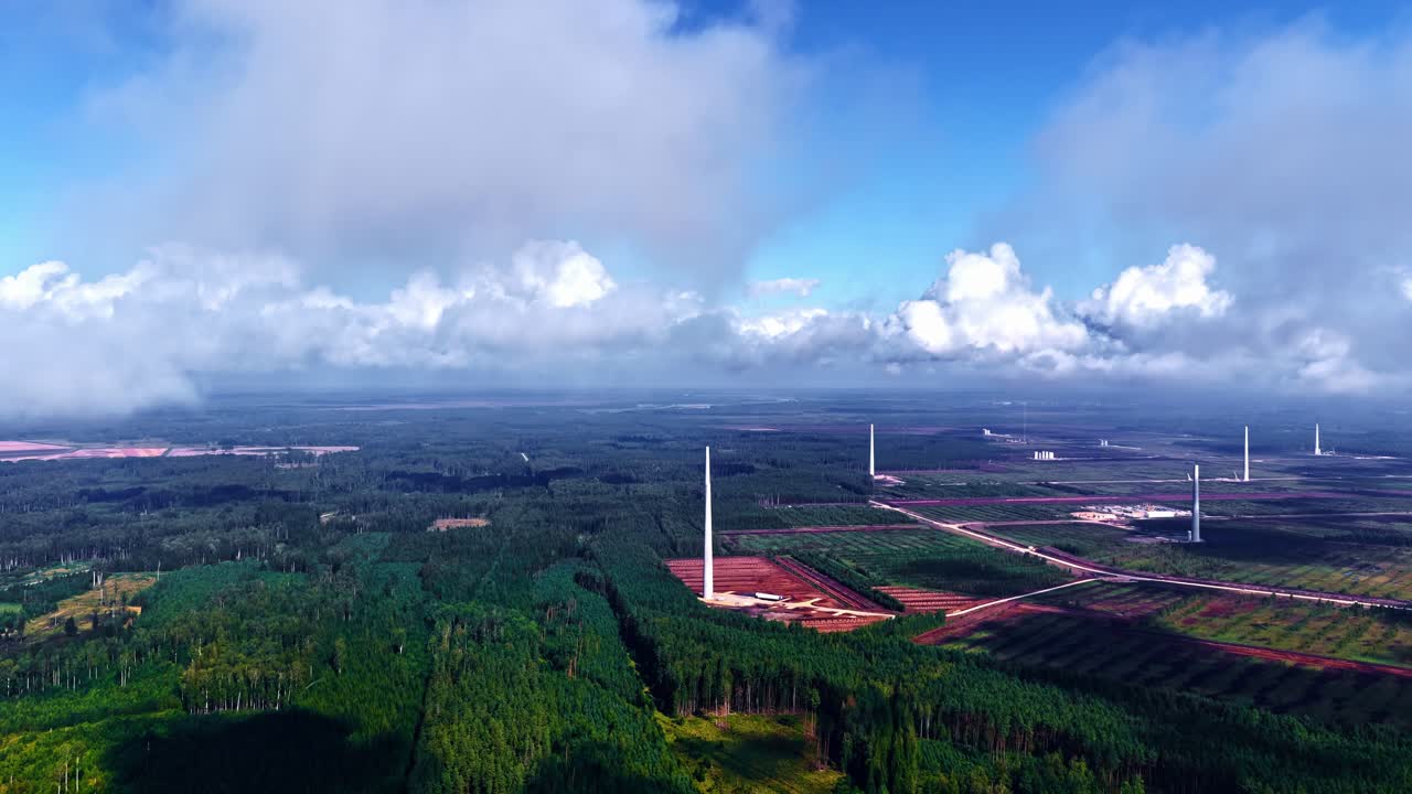 Drone shot of renewable energy project showing several tall white wind turbine towers standing on green fields in Latvia
