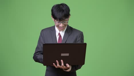 젊은 행복 한 아시아 사업가 가 노트북 을 사용 하면서 미소 짓고 있다