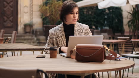 mujer de negocios trabajando en una computadora portátil en un café al aire libre.