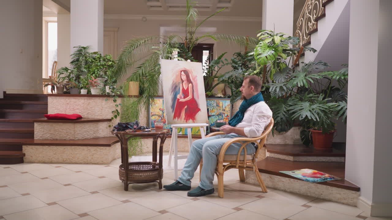 컵을 들고 있는 여자의 초상화: 숙련된 화가가 뜨거운 음료를 마시기 위해 휴식을 취하고 미술 스튜디오에서 걸작을 만드는 과정을 평가합니다.