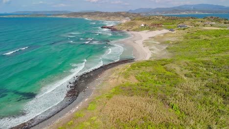 a static aerial shot captures the stunning beauty of a japanese coastline, featuring vibrant turquoise water, a white sand beach, a rocky shore, and lush green hills under a partly cloudy sky
