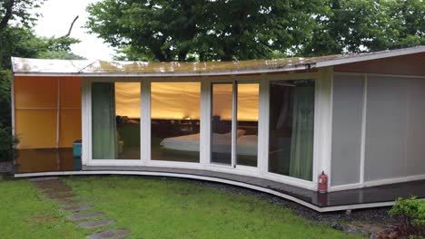 fachada de moderna villa de lujo glamping en la naturaleza con pared de vidrio curva en un día de lluvia - resort libre de glam