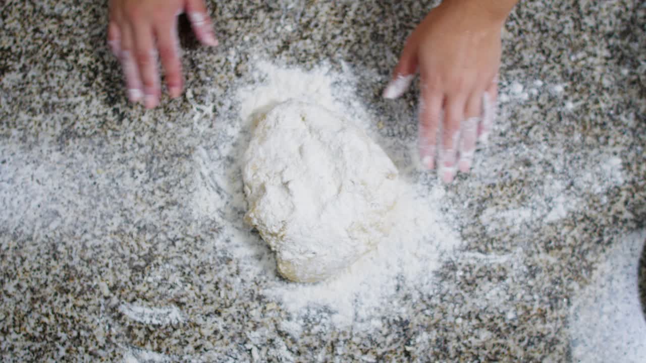 Top view of a woman dusting and kneading dough ball in a kitchen setting.