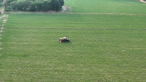 aerial drone follow tracking a tractor equipped with a boom sprayer operating within a dense maize field, highlighting precise crop treatment methods and the uniformity of modern rural agriculture