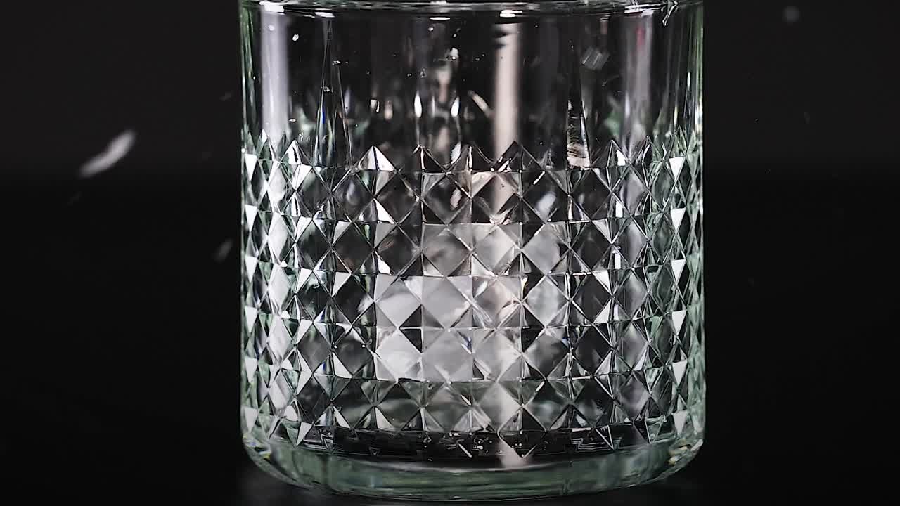 Slowmotion-optagelse af isterninger, der falder ned i et mønstret glas mod en mørk baggrund