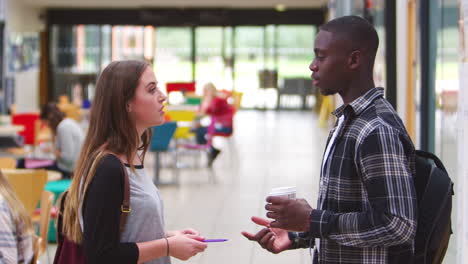 una pareja de estudiantes hablando en un área común de un campus universitario ocupado.