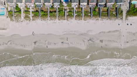 Toma-Aérea-De-Arriba-Hacia-Abajo-De-Una-Playa-De-Arena-Con-Gente-Caminando-Y-Alcanzando-Olas-En-La-Playa-De-Surf-En-Carolina-Del-Sur