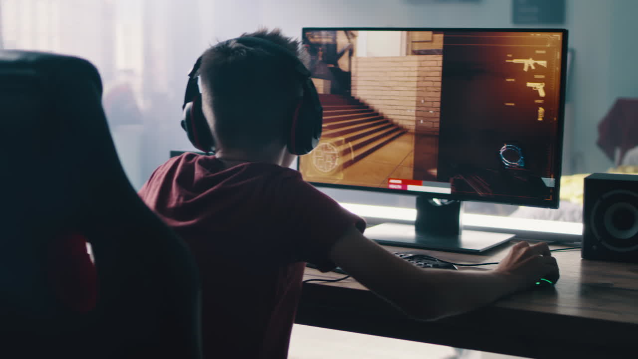 Teenage boy playing a first-person shooter video game on a computer.