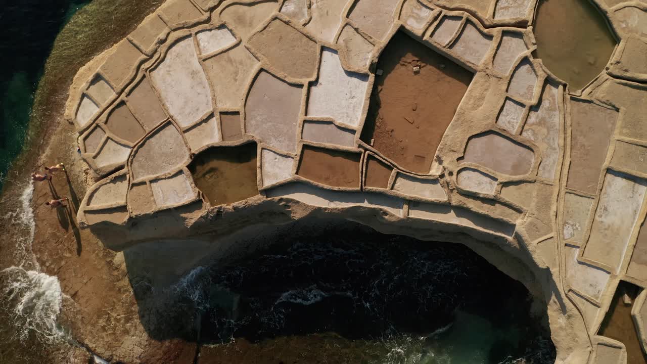 zoom aéreo de gran ángulo en toma de personas que van a nadar en el mar cerca de piscinas de salinas en xwejni durante una hermosa puesta de sol