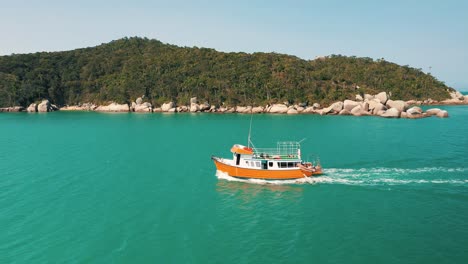 Cinematic-aerial-shot-of-a-tourist-boat-passing-by-on-turquoise-water-color-and-brazilian-paradisiac-rainforest-beach-scenery-sea