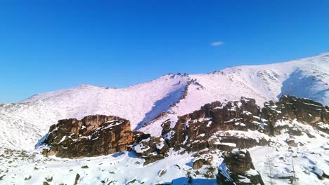 Vertical-watering-of-a-drone-near-a-mountain-with-rocks-against-a-blue-sky