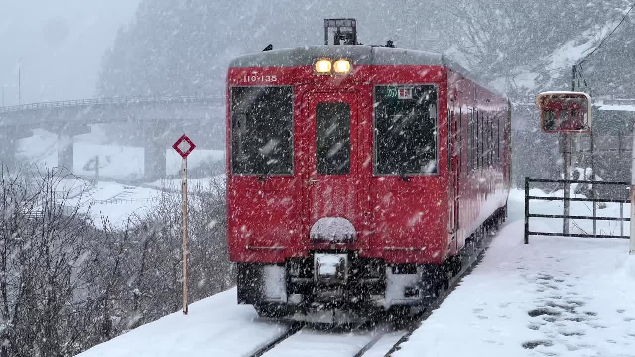 Bellissimo treno rosso che entra in stazione nella campagna rurale giapponese innevata.