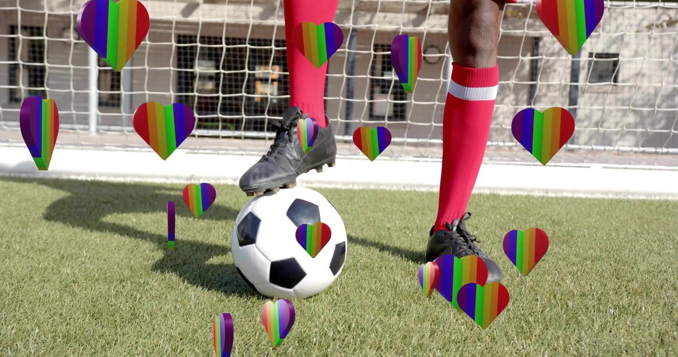 Atleta di calcio che palleggia dopo essere rotolato sull'erba sintetica, con cuori arcobaleno, per l'allenamento sportivo.