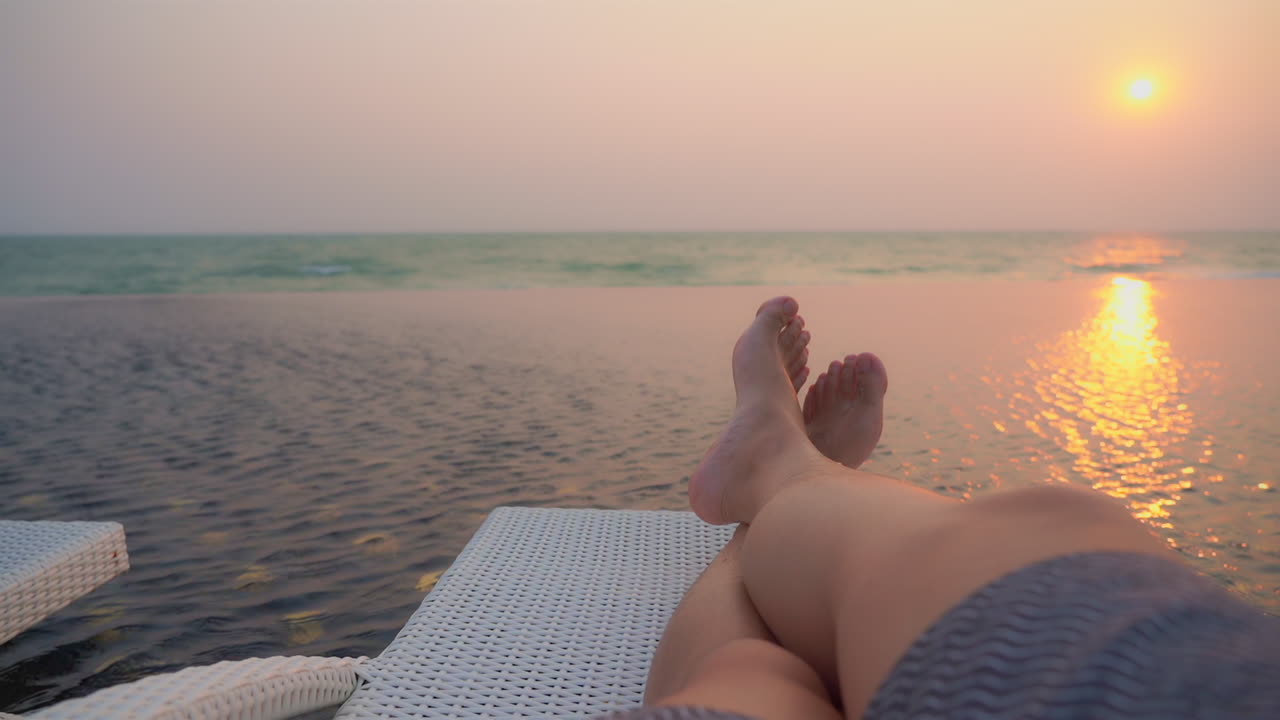 Punto di vista di un uomo sdraiato su una sedia a sdraio con una vista mozzafiato sul tramonto sul mare, gambe incrociate