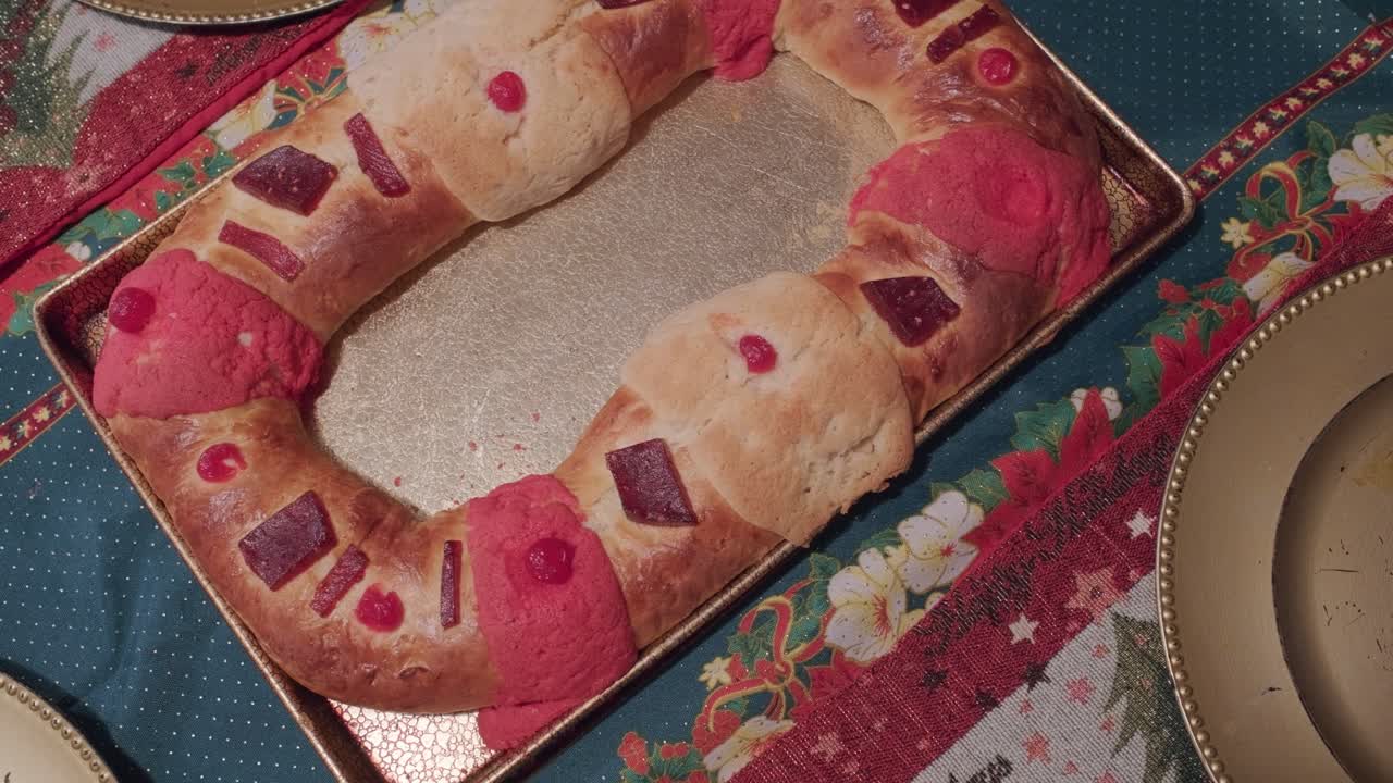 Lady placing a rosca de pastry on a decorated table with empty plates around it. Top down view