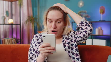 woman smiling and looking at her phone on the couch in her living room