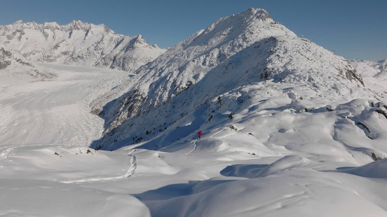 toma aérea en suiza con una persona caminando con raquetas de nieve en un día soleado con un glaciar detrás