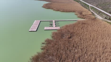 flying over lake and fishing platform next to field of grass in a sunny day | flying over field of hay next to lake | beautiful spring tall grass