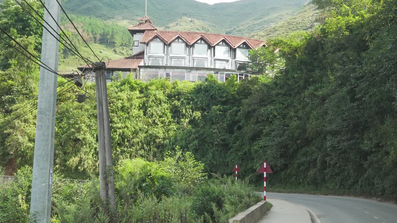 A contemporary building with peaked roofs located amid verdant foliage and rainforest on mountainside by a road, in Sapa, North Vietnam, offering a serene and picturesque environment.