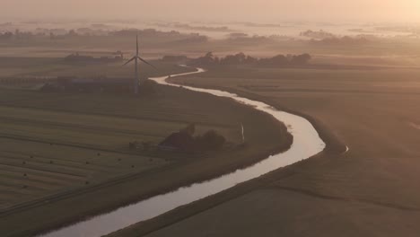 Wide-shot-of-Dutch-countryside-with-farm-and-windmill-during-sunrise,-aerial