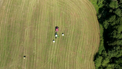 Vista-Aérea-De-Pájaro-Del-Tractor-Que-Envuelve-La-Paca-De-Heno-A-Través-Del-Campo-Verde-En-Chmielno