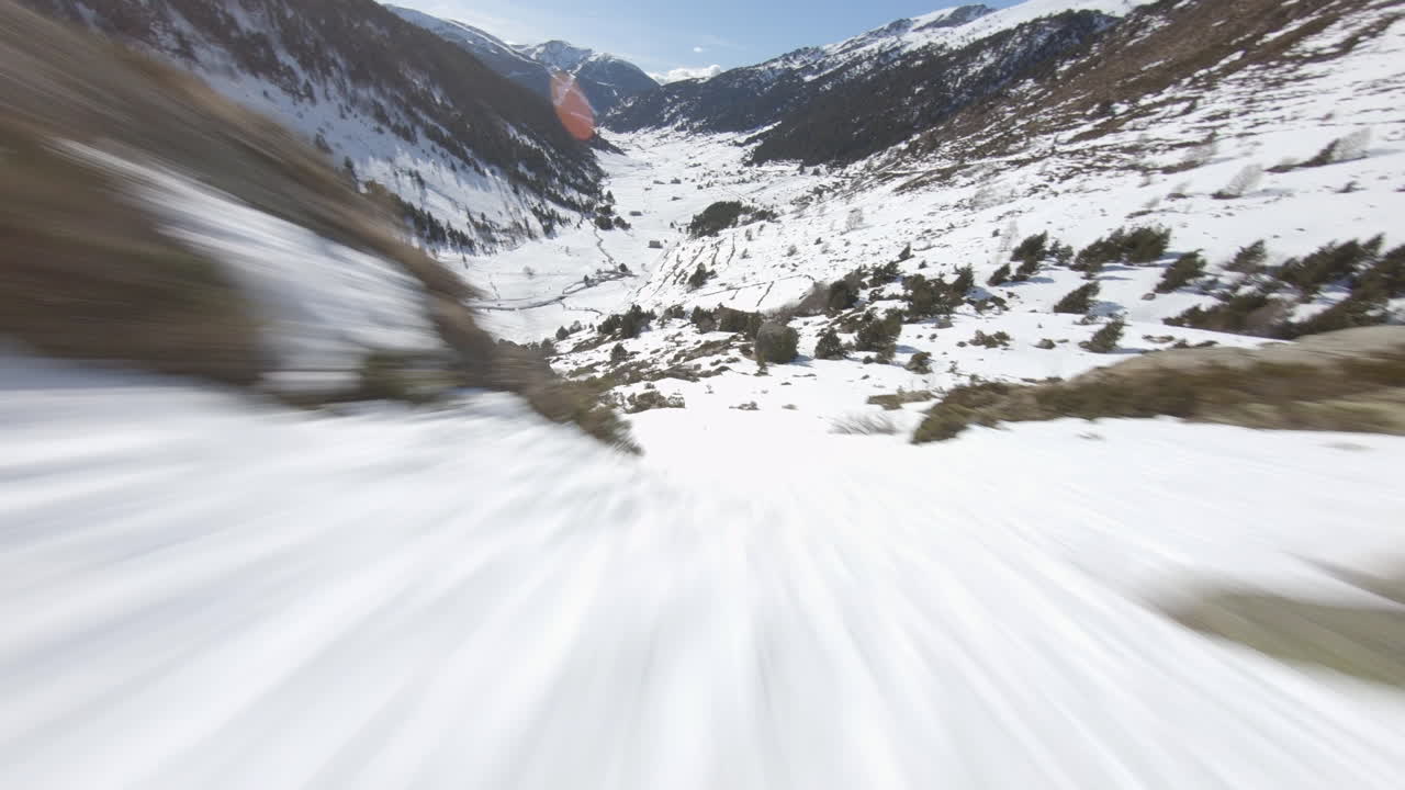 Racing drone descending towards snowy valley, Pyrenees