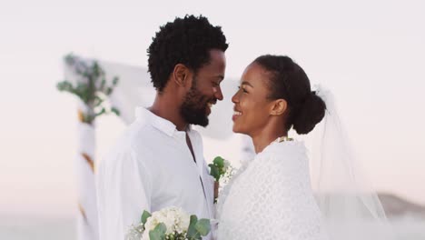 african american couple in love getting married, smiling and looking at other on the beach