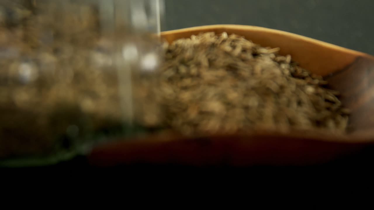 Cumin spilling out of jar into scoop 4k