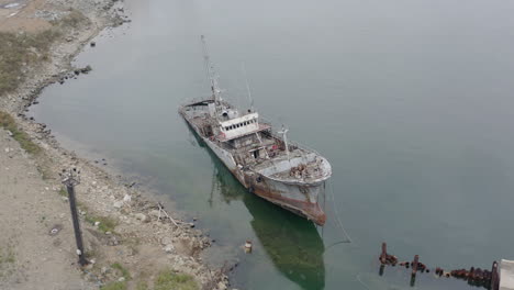 Rusty-grey-half-submerged-shipwreck-anchored-near-the-shore-on-a-cloudy-overcast-day