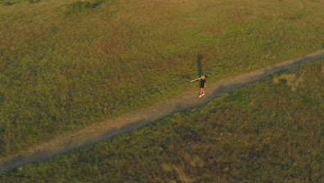 a girl walks with a shovel on her shoulders in a meadow