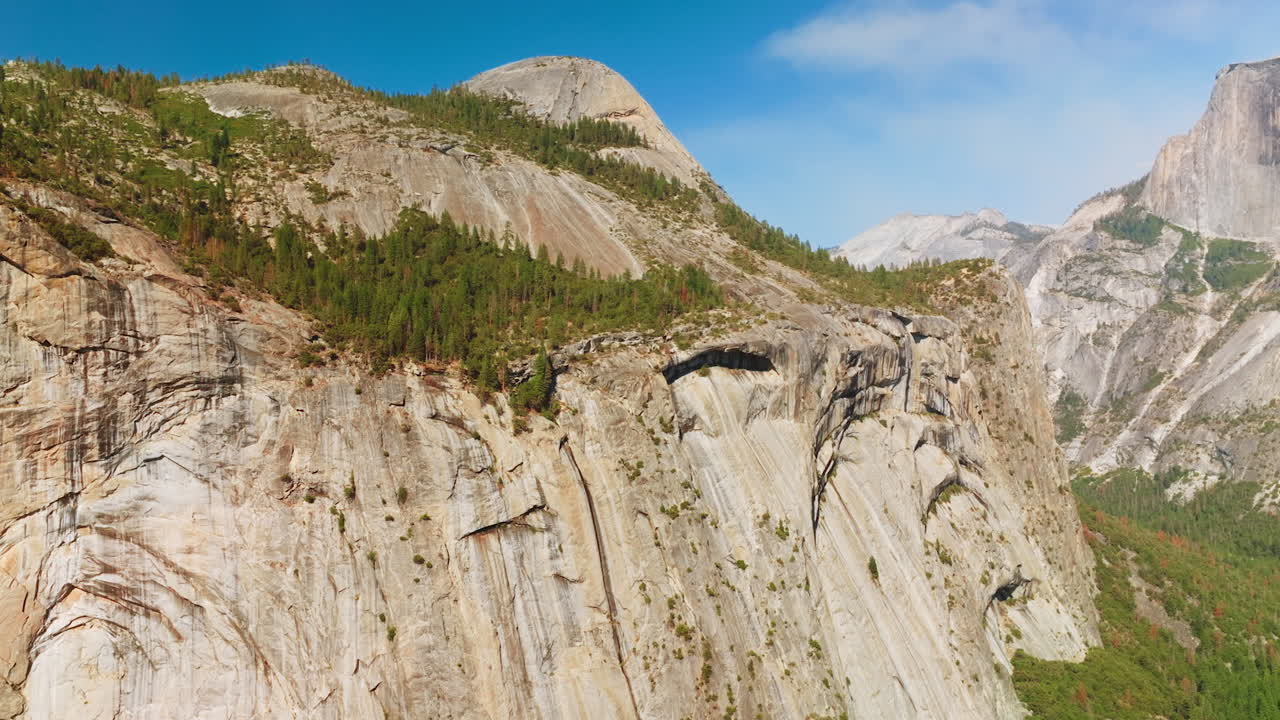 Amazing grey steep cliffs in Yosemite National Park, USA. Pine trees growing at the rocks and at the foot of mountains. Sunny day footage.