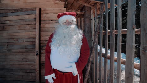 santa habla frente a una pequeña casa de madera en invierno
