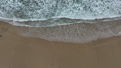 Olas-De-Agua-Espumosa-Del-Mar-Rompiendo-En-La-Playa-De-Arena---Antena-Arriba-Hacia-Abajo