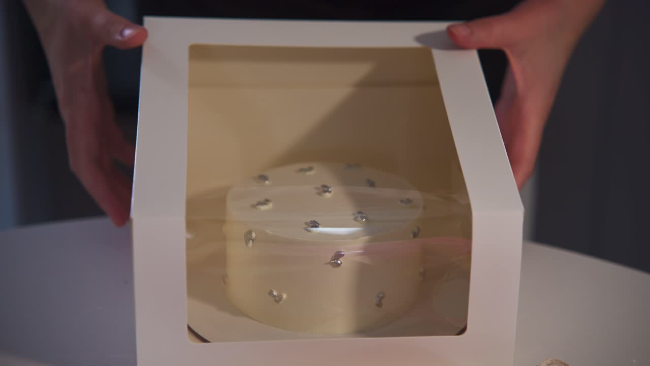 Hands Closing a White Cake Box and Adding a Pink Ribbon