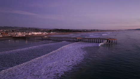 Panning-to-the-right-drone-shot-of-the-pismo-beach-pier-at-dusk-with-waves