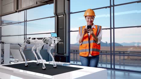 cuerpo lleno de ingeniera asiática con casco de seguridad usando teléfono inteligente mientras está de pie en una fábrica de alta tecnología, analizando el concepto de máquina robótica