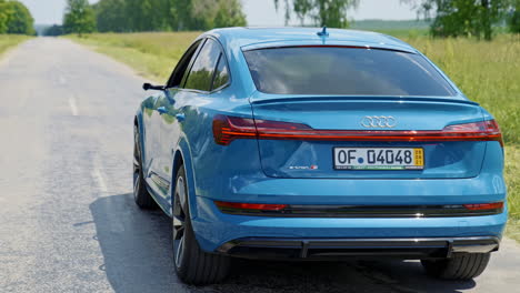 beautiful blue audi with highlights on in daytime. e-tron luxury car model driving on a highway. expensive electronic car on a road.