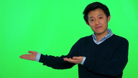 a young asian man presents something - green screen studio