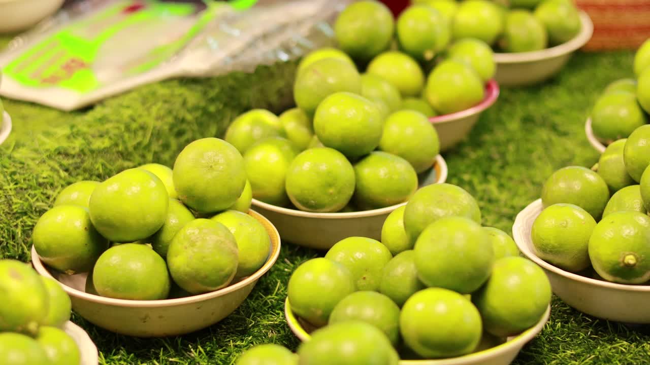 Bowls of fresh limes arranged on green turf, captured with bright lighting and vivid colors at a bustling market