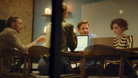 coworkers sitting table with computers in boardroom. people talking in office.