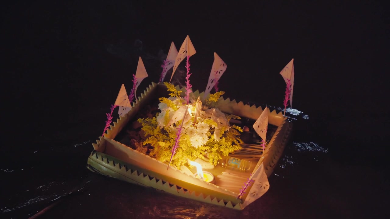 Um krathong iluminado flutua ao longo de um rio escuro em Chiang Mai, Tailândia