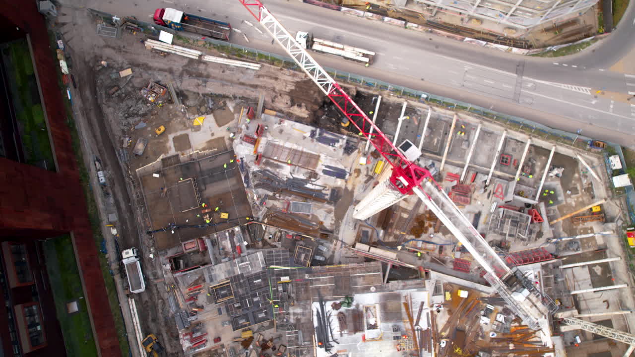 Bird's-eye view of a bustling construction site with towering cranes, machinery, and a city street alongside