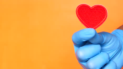 mano con guantes sosteniendo un corazón rojo