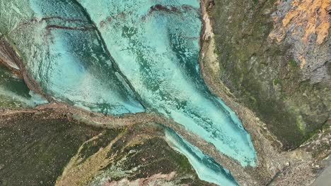 dron aéreo con un movimiento lento giratorio y ascendente a la derecha, capturando la base de grænihryggur y el río glacial, la roca verde en landmannalaugar, islandia, tonos medios de naranja y verde