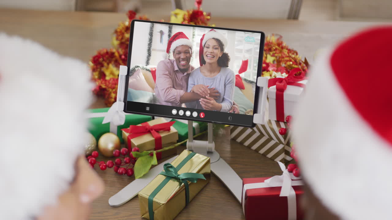 animación de una pareja diversa con sombreros de santa en una llamada de video de tableta con una pareja en navidad