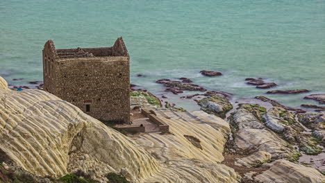 Tiro-De-Timelapse-De-Turistas-Recorriendo-Punta-Bianca,-Agrigento-En-Sicilia-Italia-A-Lo-Largo-De-La-Playa-Con-Antiguas-Ruinas-De-Una-Casa-De-Piedra-Abandonada-En-Acantilados-Blancos