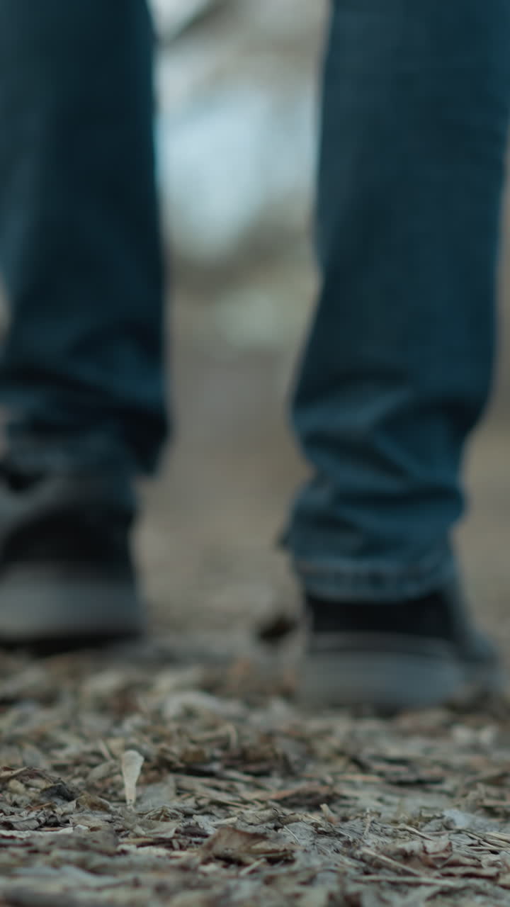 primer plano de los pies de una persona con zapatillas negras caminando por un sendero forestal cubierto de hojas