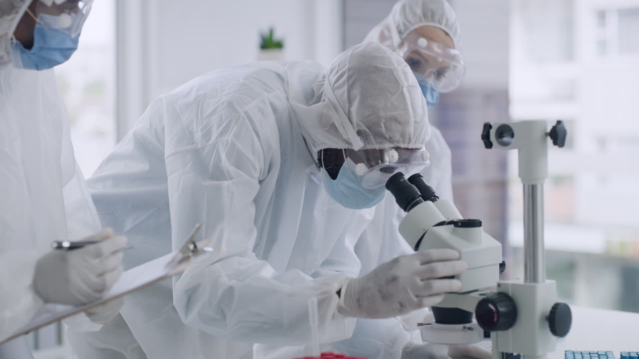 Scientists in hazmat suits using a microscope